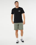 Man wearing a black t-shirt with a logo and green shorts on a white background