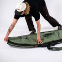 Person holding a green surf board bag on a white background