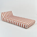 A low-profile outdoor daybed with a chaise lounge backrest, upholstered in a terracotta pink and white striped fabric, shown on a seamless light gray studio background.