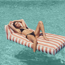 Woman in a black bikini lying on a striped pool float in clear blue water